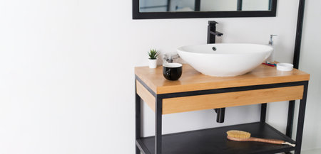 Minimalist modern bathroom with mirror in black frame, sink on wooden table and white walls, copy...