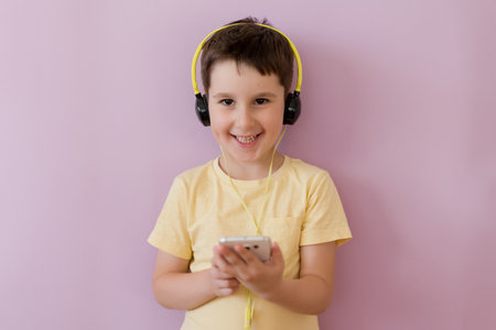 Caucasian boy in headphones holding smartphone on a pink background with copy spaceの写真素材