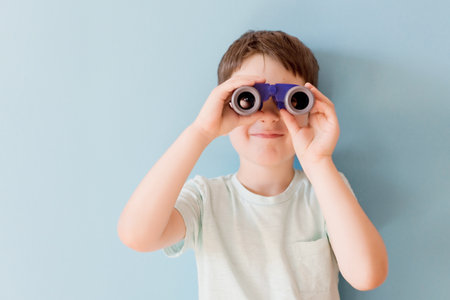 Caucasian boy with toy binoculars on a blue background with copy space. Travel funny conceptの写真素材