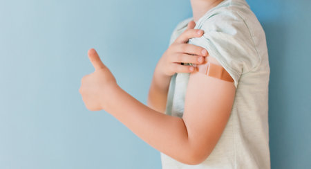 Vaccination concept. Caucasian boy in a blue t-shirt with tape thumbs up on a blue background with copy spaceの写真素材