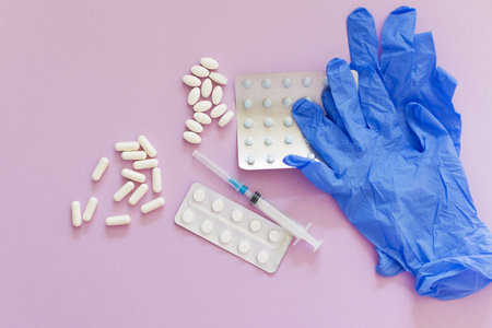 Blue gloves with assorted pills and plastic syringe on the pink background with copy space