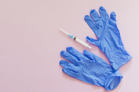 Blue gloves and plastic syringe on a pink background with copy space
