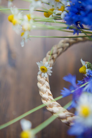 Cornflowers and chamomile in straw wicker bag on a brown wooden backgroundの写真素材