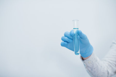 Hand in blue gloves holding test tube with blue liquid substance on a white background with copy spaceの写真素材