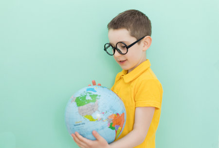 Caucasian school boy in eyeglasses holds globe on a light green background with copy spaceの写真素材
