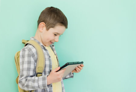 Caucasian boy with school backpack holding tablet on a green background with copy spaceの写真素材