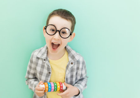 Caucasian preschool boy in eyeglasses with arithmetic math learning toy on a light green background with copy spaceの写真素材