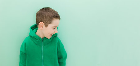 Caucasian boy in green hoodie on a light green background smiling, copy spaceの写真素材