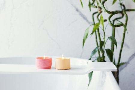 Craft pink and orange soy candles on baththube near bamboo plant at white light bathroom interiorの写真素材