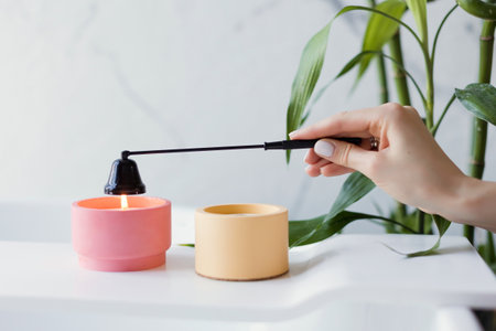 Craft pink and orange soy candles on baththube near bamboo plant at white light bathroom interior. Woman extinguish candle with black candle snufferの写真素材