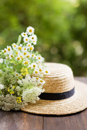 Straw hat boater and wildflowers bouquet on a wooden table on green backgroundの写真素材