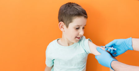 Vaccination concept. Doctor in a blue gloves vaccinating caucasian boy in a blue t-shirt on an orange background with copy spaceの写真素材