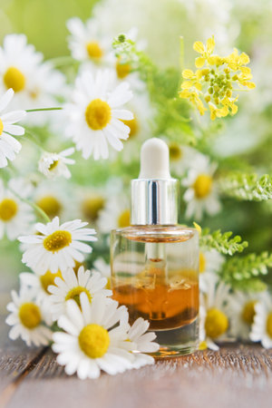 Cosmetic bottle with serum oil and chamomiles on a wooden table on a nature backgroundの写真素材