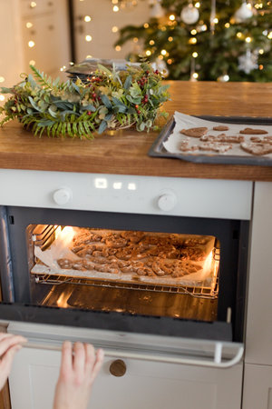 Gingerbread cookies are baked in the oven at light kitchen with Christmas decorationsの写真素材