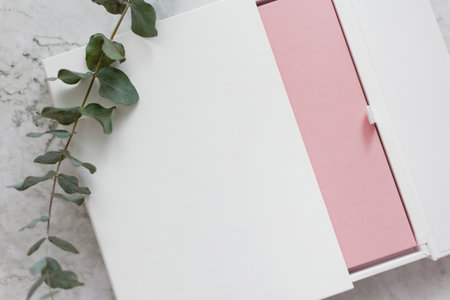 Pink cover book with copy space on a marble background and eucalyptus twig. Woman holding pink book...
