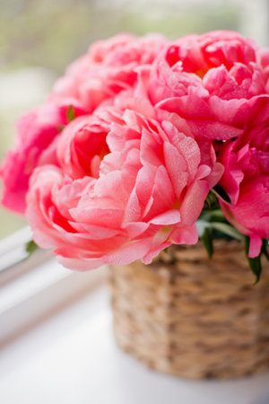 Bouquet of coral peonies in wicker basket on a windowsillの写真素材
