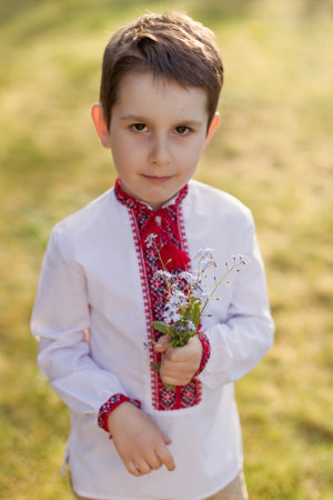 Caucasian boy in traditional ukrainian cloth vyshyvanka holds bouquet of blue flowers forget me not....