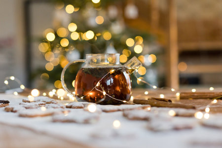 Glass teapot with black tea and gingerbread cookies on a wooden table near Christmas tree