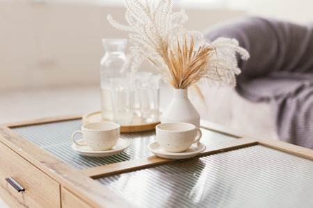 Cups and vase with dry flowers on a glass tableの写真素材