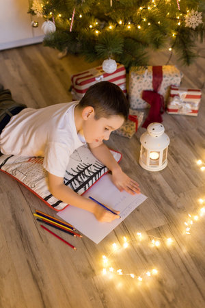 Boy lying near Christmas tree and writing letter to Santa Clausの写真素材
