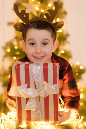 Boy in reindeer horns holding gift box near Christmas treeの写真素材