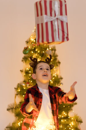 Boy in reindeer horns holding gift box near Christmas treeの写真素材