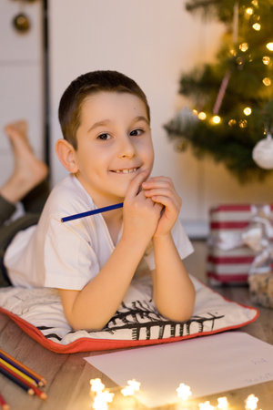 Boy lying near Christmas tree and writing letter to Santa Clausの写真素材