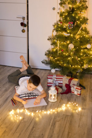 Boy lying near Christmas tree and writing letter to Santa Clausの写真素材