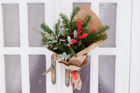 Christmas bouquet with red berries ilex, fir tree and eucalyptus on a white wooden doorの写真素材