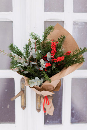 Christmas bouquet with red berries ilex, fir tree and eucalyptus on a white wooden doorの写真素材