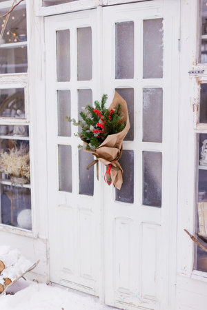 Christmas bouquet with red berries ilex, fir tree and eucalyptus on a white wooden doorの写真素材