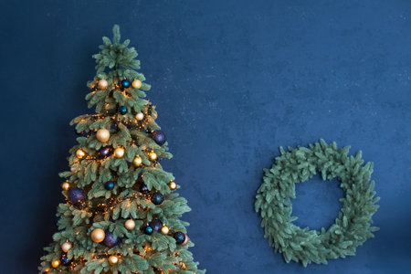 Christmas tree with golden decorations and fir tree wreath on a blue wall, copy spaceの写真素材
