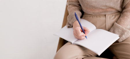 Caucasian woman in beige clothes writing in notebook indoorsの写真素材