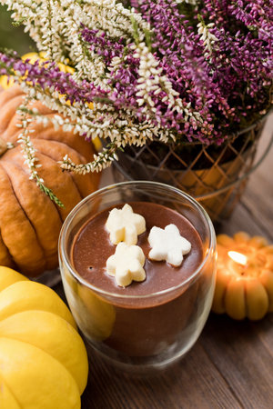 Hot chocolate in glass cup, pumpkins, burning candle and heather in pot on a wooden tableの写真素材