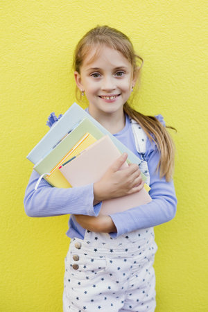 Schoolgirl with books on a yellow backgroundの写真素材