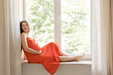 Pregnant woman relaxing by the window, enjoying peaceful momentsの写真素材