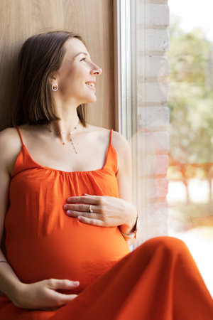 Pregnant woman relaxing by the window, enjoying peaceful momentsの写真素材