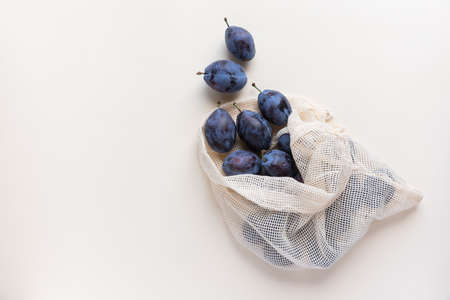 autumn harvest background with copy space: organic plums in a reusable cotton net bag on creamy...