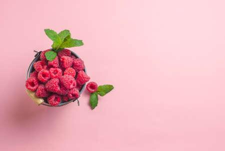 ripe raspberries in a grey bucket on pink background served as healthy seasonal dessert