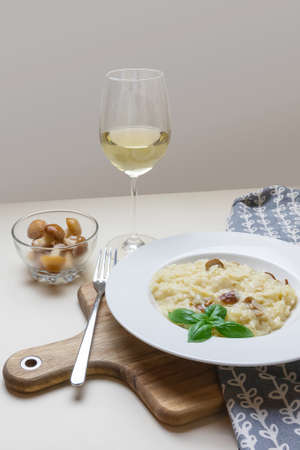 Vegetarian gourmet mushroom risotto on a white plate, yellow background, served with a glass of white wine. A northern Italian rice dish cooked with broth until it reaches a creamy consistency.の写真素材