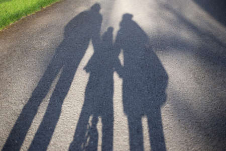 shadows of a family - mother, father and kid on a bike - on a walk outdoors in the parkの写真素材