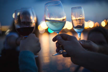 a party outside, celebrating and raising glasses with wine against blue night sky and yellow city...