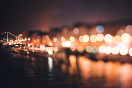 Bridge and boat going down the river in Budapest at night with selective focus, blurry city lights bokehの写真素材