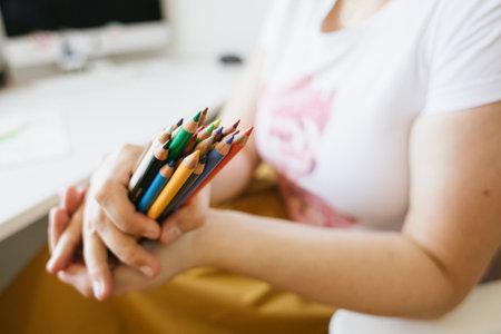 a bunch of colour pencils in womans hands , computer desk in backgroundの写真素材