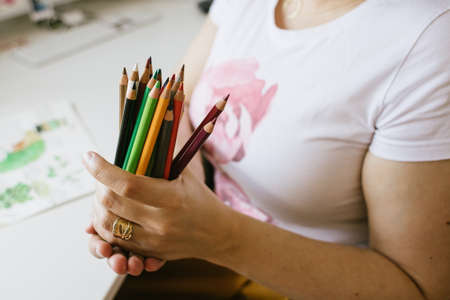 a bunch of colour pencils in womans hands , a desk with drawings in backgroundの写真素材