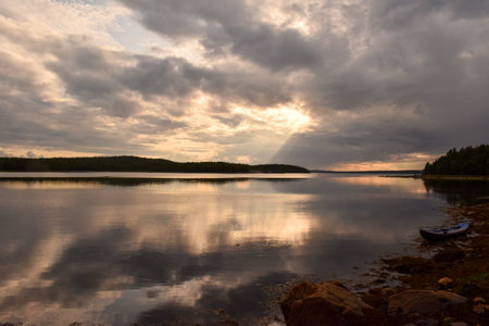 A boat sitting on the shore of a lake under a cloudy sky, flickering light, photo taken with ektachrome, anamorphic lens flareの写真素材