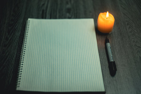 Workplace. A large notepad with a black marker lies on a wooden black table and is illuminated by a candle.. High quality photoの写真素材