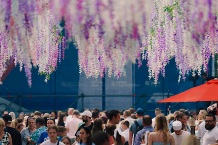 A large crowd of people enjoying an outdoor festival, with colorful floral decorations hanging overhead.の写真素材
