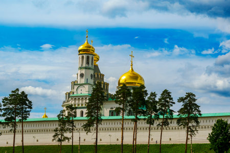 The golden domes of New Jerusalem Monastery rise above its white walls, set against a blue sky with trees in the foreground.の写真素材