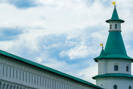 Historic monastery towers with green roofs and yellow flags under a vibrant blue sky with clouds.の写真素材